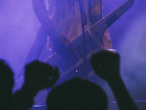 Músico tocando un keytar en un escenario de humo oscuro con gente divirtiéndose en un concierto en un club —  Fotos de Stock