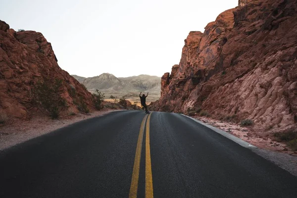 Tiro de uma pessoa patinando em uma estrada rodeada por rochas vermelhas — Fotografia de Stock
