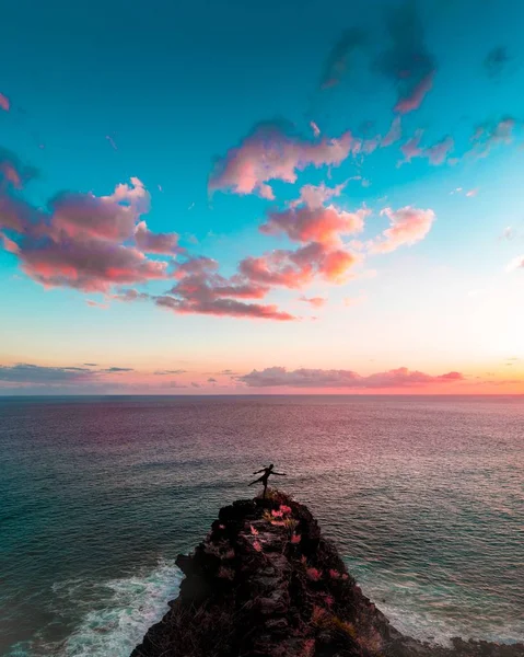Masculino de pé em rochas perto do belo mar e incríveis nuvens rosa de tirar o fôlego no céu azul — Fotografia de Stock