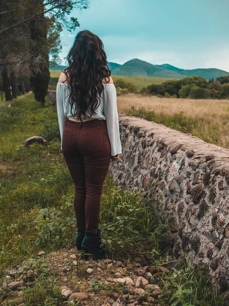 Beautiful shot of a girl with long wavy hair from behind wearing a white shirt and maroon pants