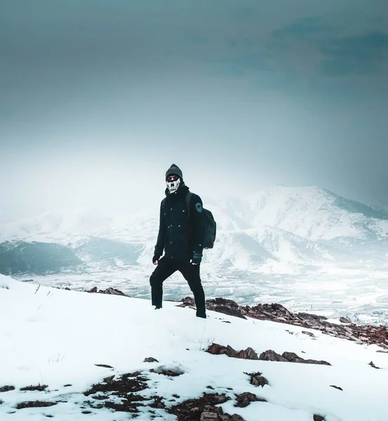 Cool wandelaar in een masker en donkere kleren alleen op een besneeuwde steile heuvel in de bergen — Stockfoto