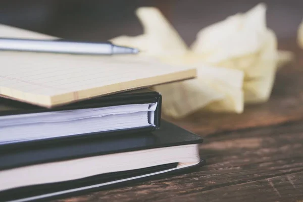 Primer plano de los libros de texto con una pluma gris y pedazos arrugados de papel alrededor de una superficie de madera — Foto de Stock