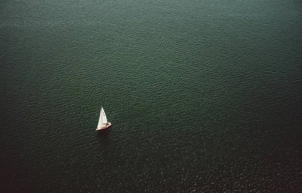 An aerial shot of a small boat sailing in the wide beautiful ocean