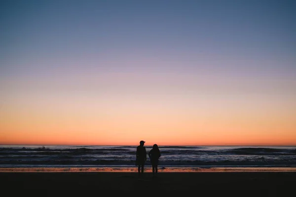 Silhouettes of a couple standing on the beach and enjoying the beautiful sunset — Stock Photo, Image