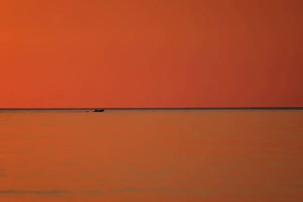 Beautiful shot of a sea with a boat sailing in the distance and an orange sky at sunset — Stock Photo, Image