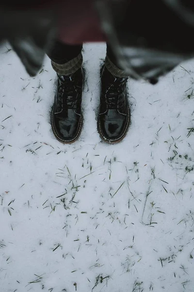 Vertical shot of a person wearing black boots standing on snow shot from above — 스톡 사진