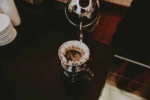 Closeup of a cup of coffee on the table with a person pouring liquid sugar from a kettle on it