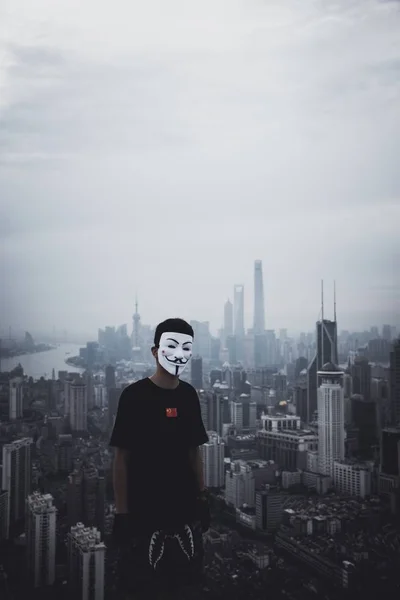 Male wearing an anonymous mask standing on a roof with an amazing urban city in the back — Stock Photo, Image