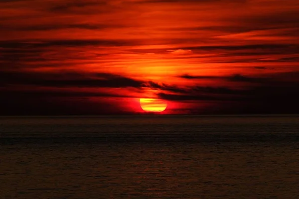 Belo tiro de um mar e sol atrás das nuvens ao pôr do sol — Fotografia de Stock