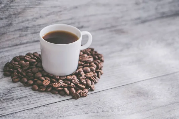 Primer plano de una taza de café en granos de café en forma de corazón sobre una superficie de madera — Foto de Stock