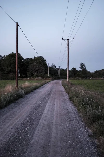 Tiro vertical de uma estrada de cascalho no campo com postes de eletricidade nas laterais — Fotografia de Stock