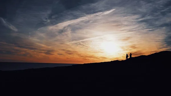 Gros plan de silhouettes de deux personnes marchant sur une colline avec le soleil qui brille en arrière-plan — Photo