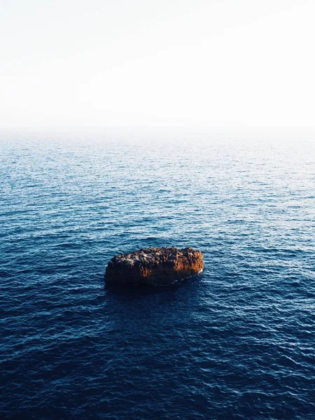 Wunderschöne vertikale Aufnahme eines braunen Felsens mitten im Meer mit erstaunlichen Wasserstrukturen — Stockfoto