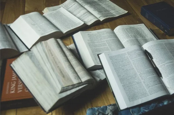 Closeup tiro de livros abertos com uma caneta e a Bíblia sagrada no lado em uma superfície de madeira — Fotografia de Stock