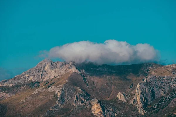 Bellissimo scatto di una nuvola sopra la montagna in lontananza con un cielo azzurro chiaro sullo sfondo — Foto Stock