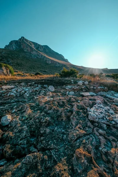 Vertikale Aufnahme von Felsen in der Nähe eines trockenen Grasfeldes mit einem Berg und einem klaren blauen Himmel im Hintergrund — Stockfoto