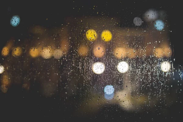 Primo piano delle gocce di pioggia su una finestra di vetro trasparente con luci sfocate sullo sfondo — Foto Stock