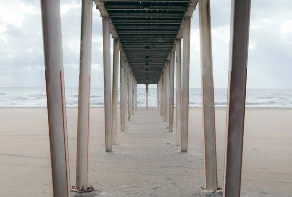 Debajo de un muelle de madera en la playa de arena en un día nublado —  Fotos de Stock