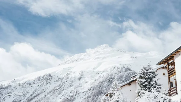 Bred bild av ett vitt och brunt hus nära träd och ett berg täckt av snö — Stockfoto