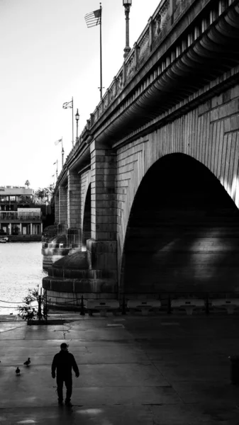 Preto e branco tiro de um homem de pé ao lado de uma grande ponte de pedra — Fotografia de Stock