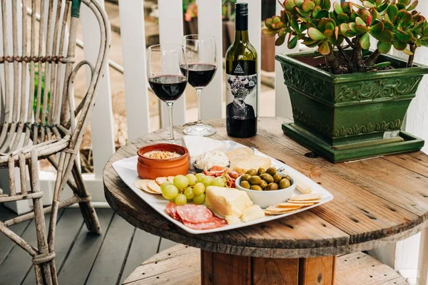 Owoce i mięso w pobliżu kieliszków do wina i butelki na drewnianym stole z doniczką — Zdjęcie stockowe