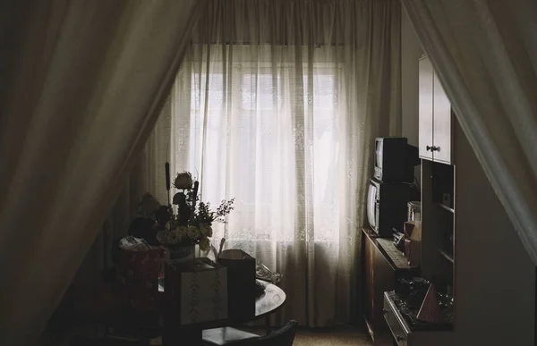 Tiro de um armário, TV, cortina perto de uma mesa com um vaso de flores nele em um quarto — Fotografia de Stock