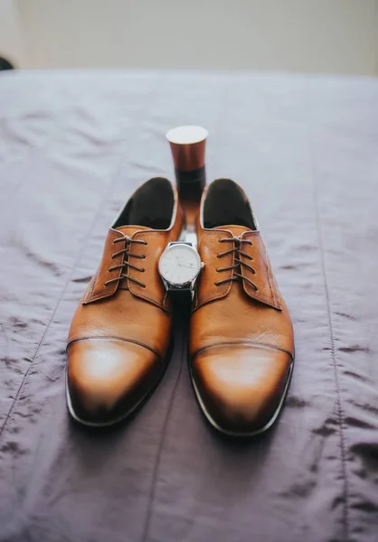 Vertikale Aufnahme brauner klassischer Schuhe auf grauem Laken mit einer Uhr dazwischen — Stockfoto