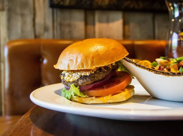 Крупним планом гамбургер з м'ясом, вкритим золотом біля салату на білій тарілці — стокове фото