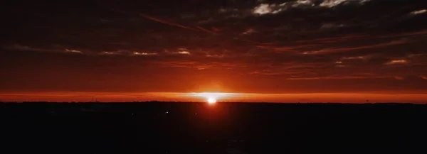 Schöne Panoramaaufnahme der dunklen Hügel mit der Sonne am Horizont bei bewölktem Himmel — Stockfoto
