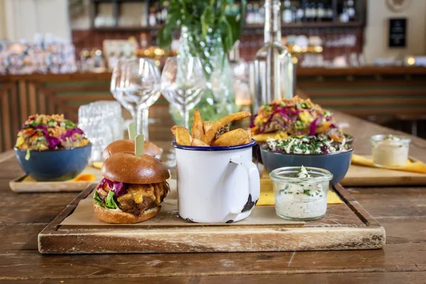 Un trago de hamburguesa cerca de papas fritas en una taza y una salsa en una bandeja de madera — Foto de Stock