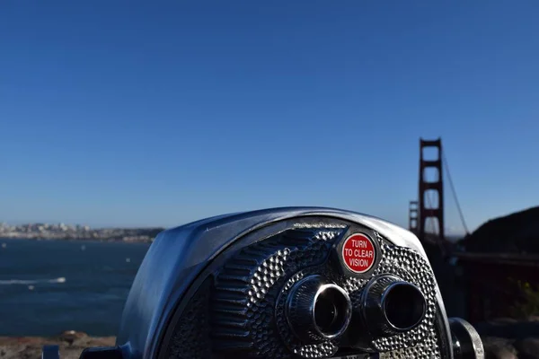 Selective closeup shot of a tourist telescope on the blurry background of the Golden Gate Bridge — Stock Photo, Image