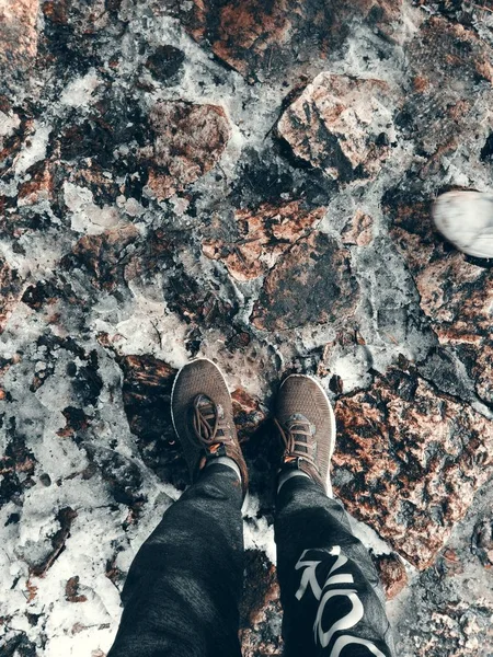 Vertikalt skott av en persons fötter på en snöig och stenig mark — Stockfoto