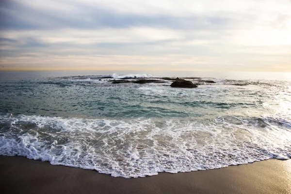 Прекрасний знімок морських хвиль, що падають на берег скелями на відстані під хмарним небом — стокове фото