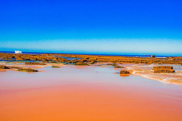 Lindo tiro de uma praia de sobrancelha com água no lado e pedras sob um céu azul claro — Fotografia de Stock