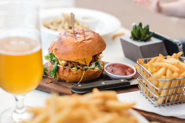 Selective closeup shot of french fries, ketchup and burger on a wooden board — Stock Photo, Image