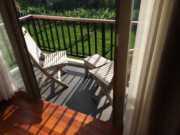 Piękny strzał drzwi do balkonu z drewnianymi krzesłami w pobliżu ogrodzenia metalu nad trawiaste pole — Zdjęcie stockowe
