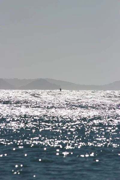 Вертикальный снимок красивого моря с солнцем, отражающимся на воде, и человеком на лодке — стоковое фото