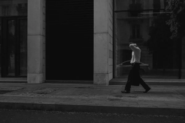 Πυροβολισμός από διαβαθμίσεις του γκρι ενός αρσενικού που περπατούσε κατά μήκος μιας πεζοδρομημένης ζώνης κοντά σε ένα κτίριο — Φωτογραφία Αρχείου