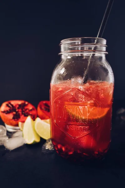 Colpo verticale di una tazza di vaso di vetro riempita con succo di melograno con una cannuccia su uno sfondo nero — Foto Stock