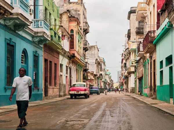 Amplio plano de un hombre afroamericano caminando por una carretera con autos cerca de coloridos edificios en La Habana —  Fotos de Stock