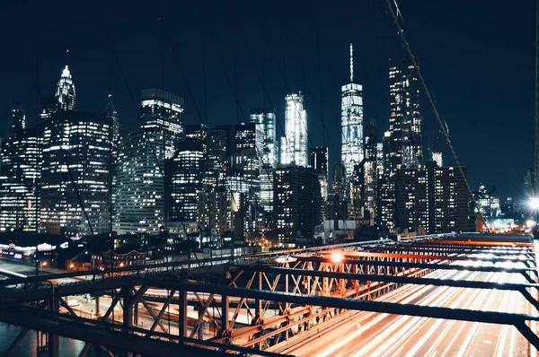 Wide shot of skyscrapers and the Brooklyn Bridge above a road in New York during nighttime — Stock Photo, Image