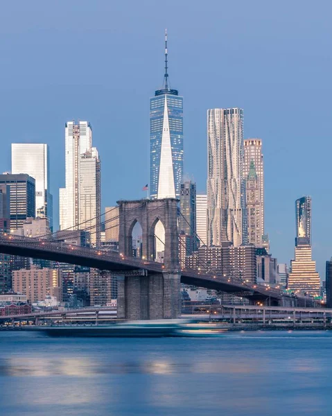 Colpo verticale distante del ponte di Brooklyn sul corpo d'acqua vicino ai grattacieli di New York — Foto Stock