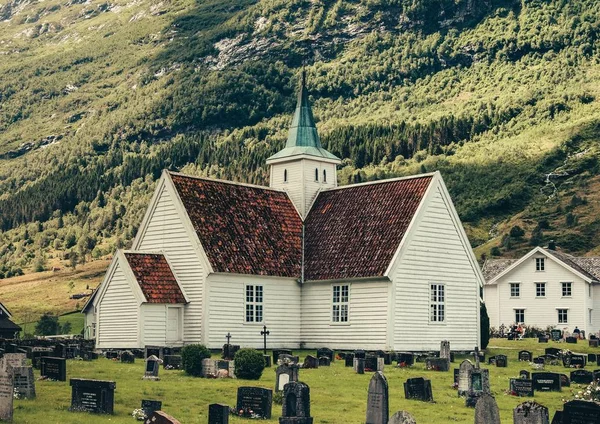 Bred bild av en kyrka med en kyrkogård full av gravstenar och gröna kullar i bakgrunden — Stockfoto