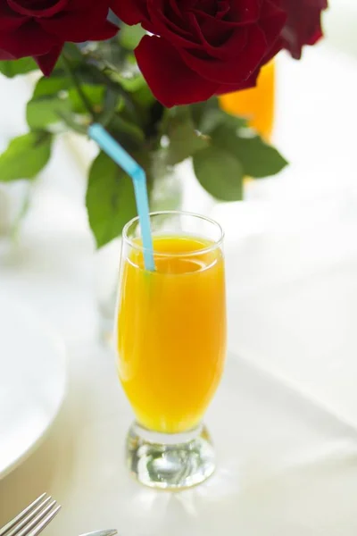 Primo piano verticale selettivo ha sparato un succo d'arancia in un bicchiere da bere sullo sfondo di rose rosse — Foto Stock