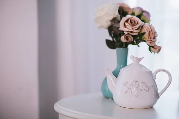 Primer plano selectivo de una tetera de cerámica blanca cerca de un jarrón azul con rosas rosadas sobre una mesa blanca —  Fotos de Stock