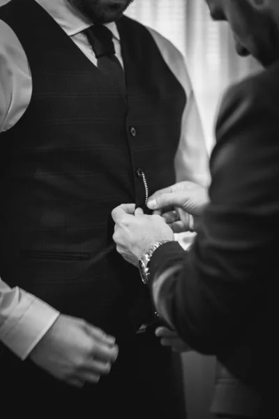 Balança de cinza vertical de um macho abotoando o casaco de seu amigo para o casamento — Fotografia de Stock