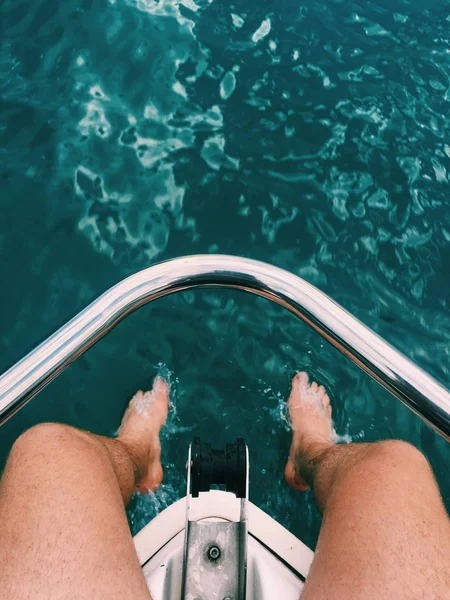 Verticaal schot van een persoon die aan de rand van de boot zit met zijn voeten in het water — Stockfoto