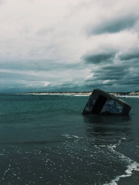 Vertikale Aufnahme eines grauen quadratischen Objekts, das unter wolkenverhangenem Himmel auf dem Wasser schwimmt — Stockfoto