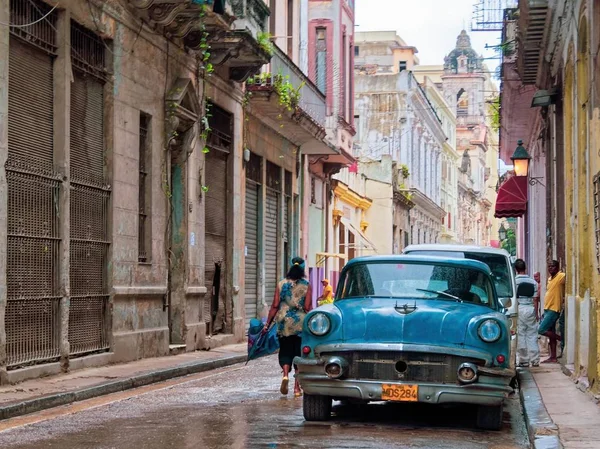Szeroki strzał niebieski samochód zaparkowany na ulicy w pobliżu budynków i ludzi w Hawanie Vieja, Kuba — Zdjęcie stockowe
