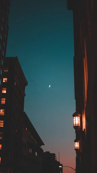 Bella foto ad angolo basso degli edifici di notte con una mezza luna splendente nel cielo blu della sera — Foto Stock